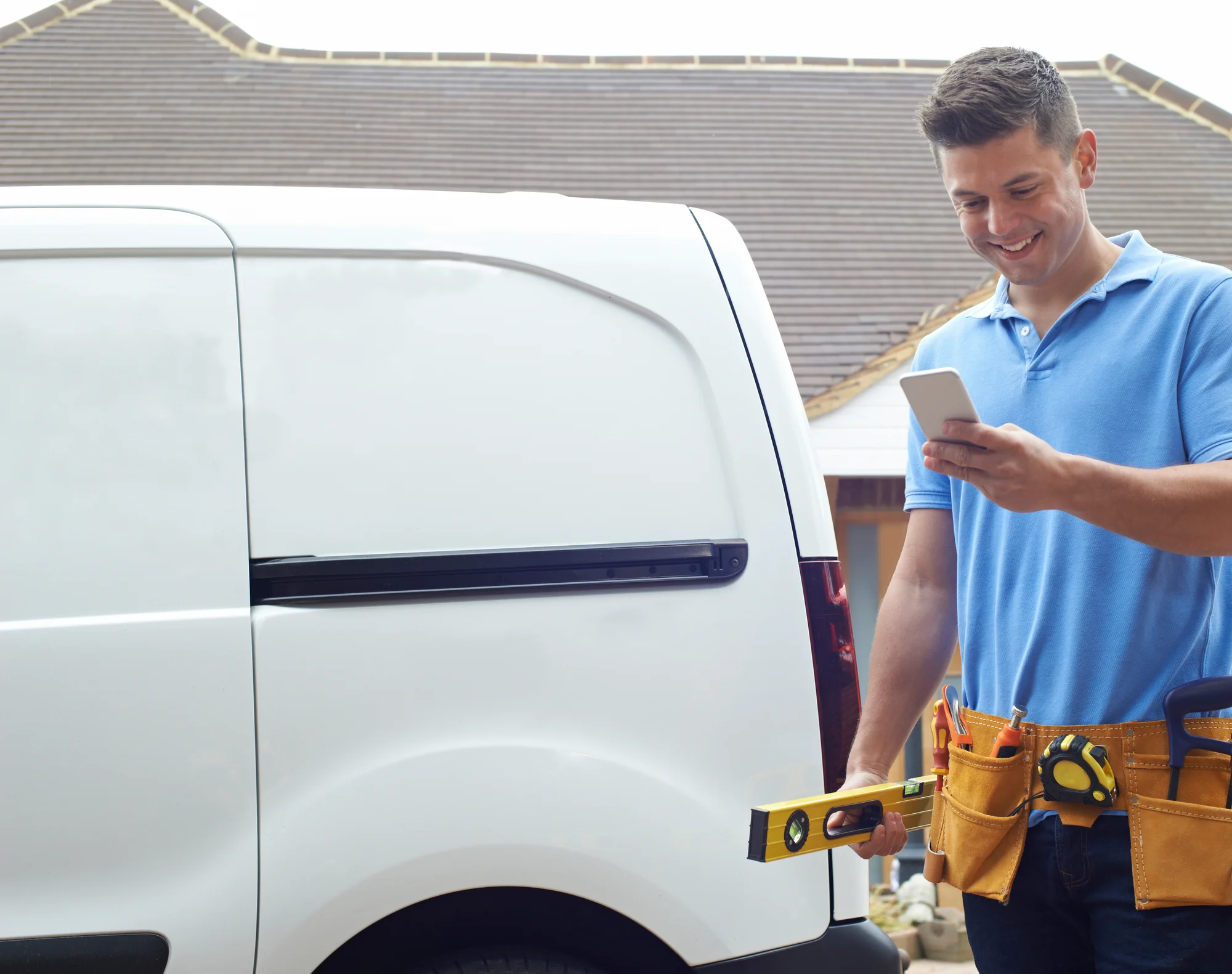UK tradesperson checking job details on phone next to van